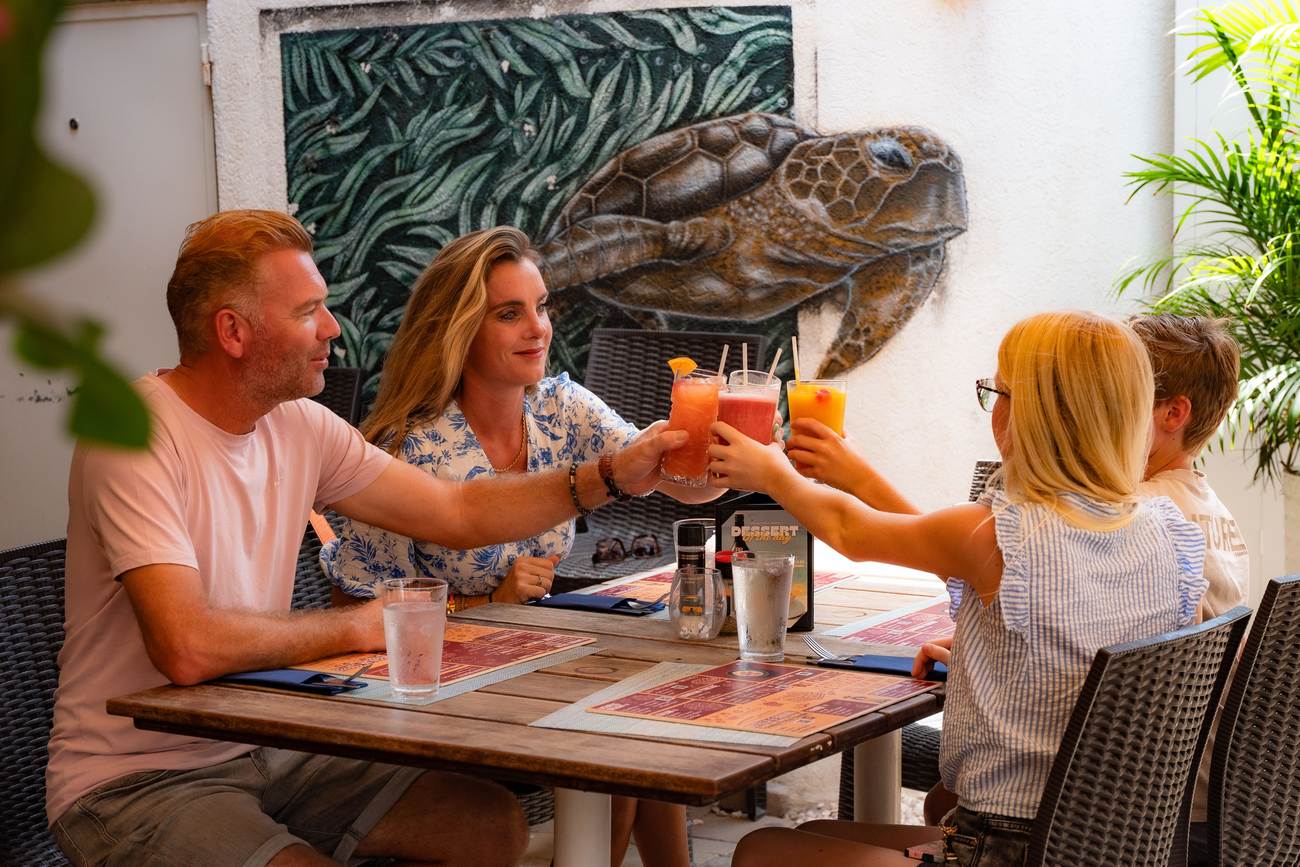 A family toasting fresh juices on the terrace at Crazy Pancakes Aruba under the sea turtle mural
