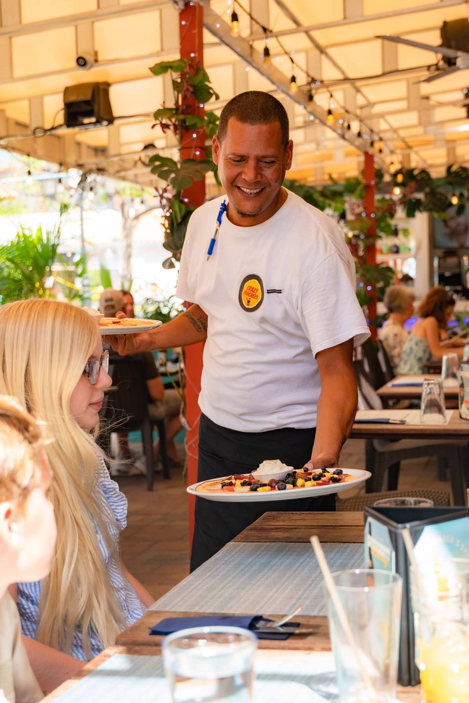 A Crazy Pancakes waiter serving a fresh fruit pancake on the terrace
